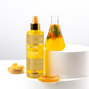 Tónico aclarante capilar natural de 250 ml en botella amarilla con spray dorado, acompañado de polvo, flores en infusión y una plataforma cilíndrica blanca.